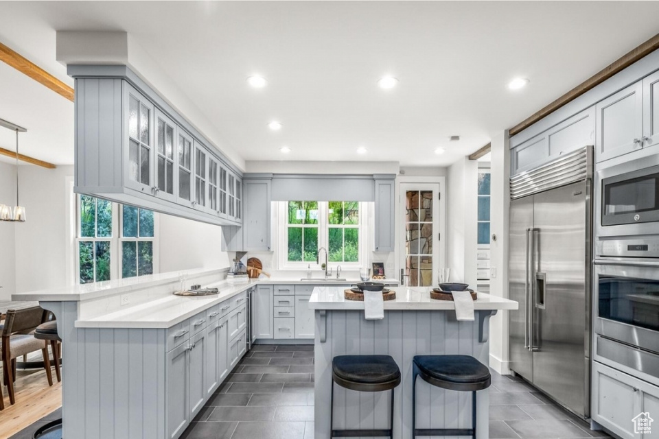 Kitchen featuring a sink, a kitchen breakfast bar, a peninsula, light countertops, and built in appliances