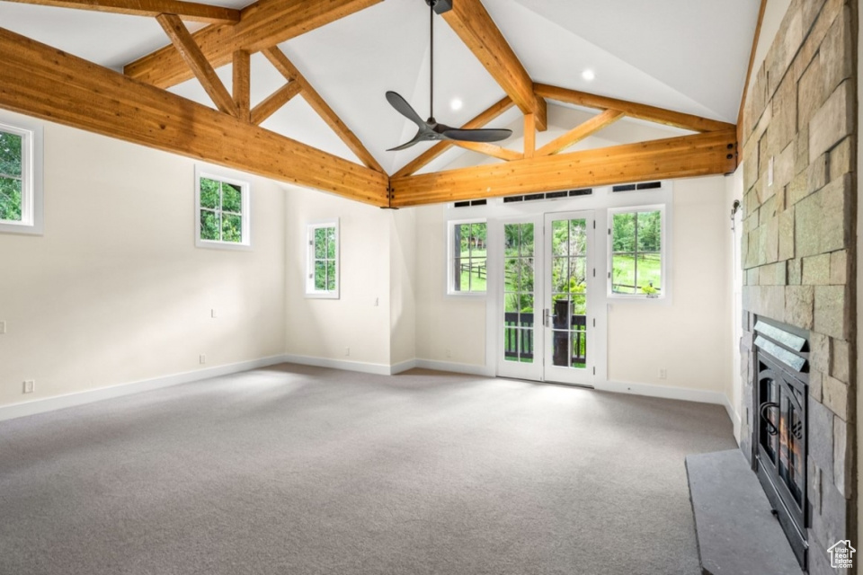 Unfurnished living room with carpet, baseboards, ceiling fan, a stone fireplace, and beamed ceiling