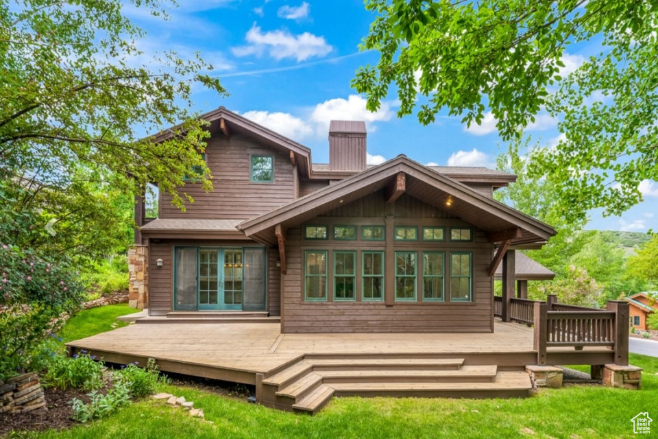 Rear view of house featuring a deck, a lawn, and a chimney