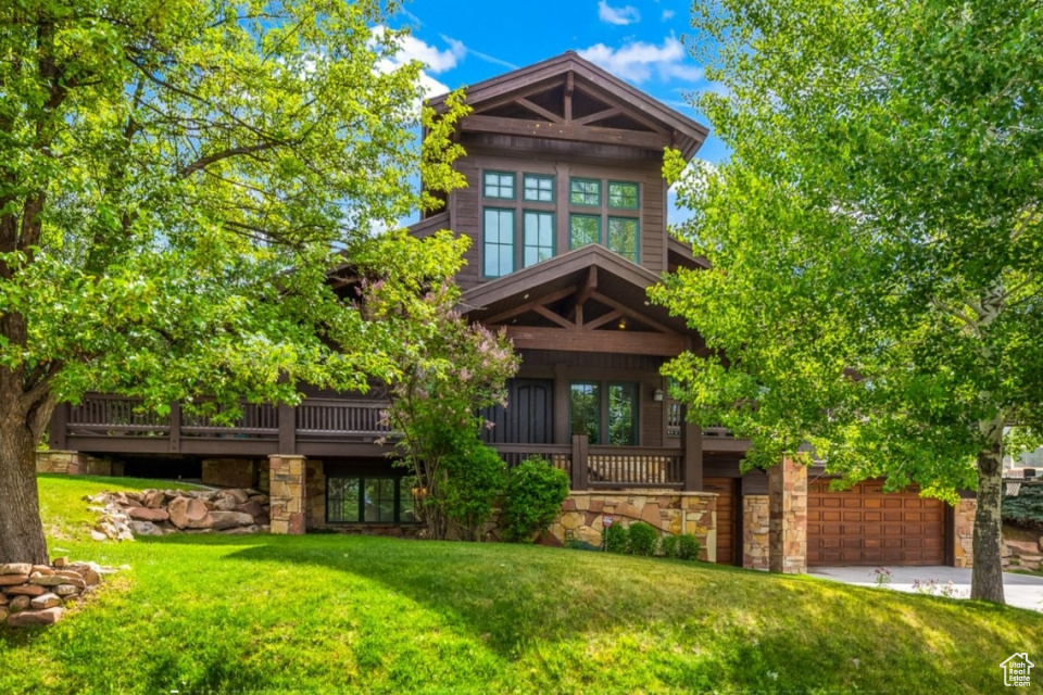 View of front of house with stone siding, driveway, and a front lawn