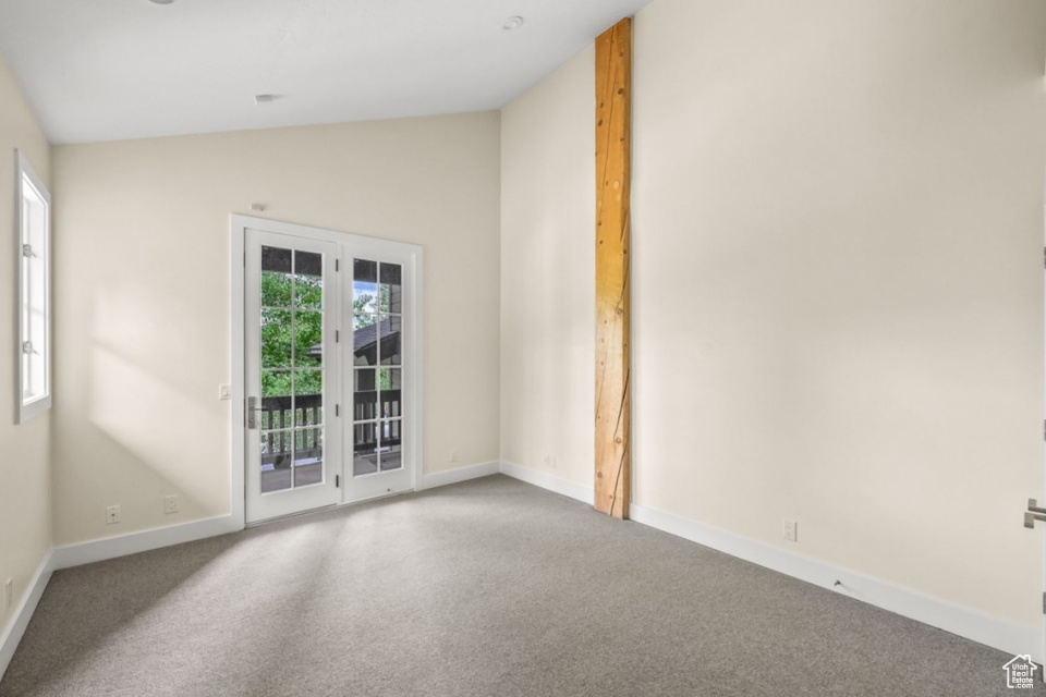 Carpeted empty room featuring vaulted ceiling and baseboards