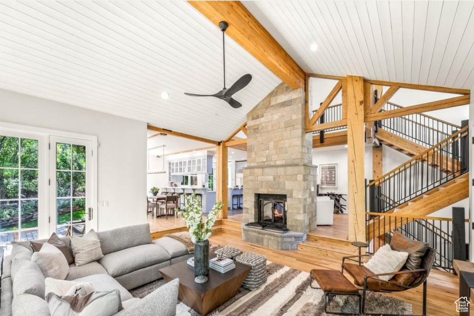 Living room featuring beamed ceiling, a ceiling fan, wood finished floors, a stone fireplace, and stairs