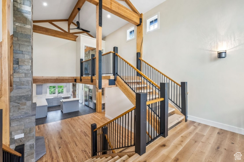 Staircase featuring beam ceiling, high vaulted ceiling, a wealth of natural light, and wood finished floors