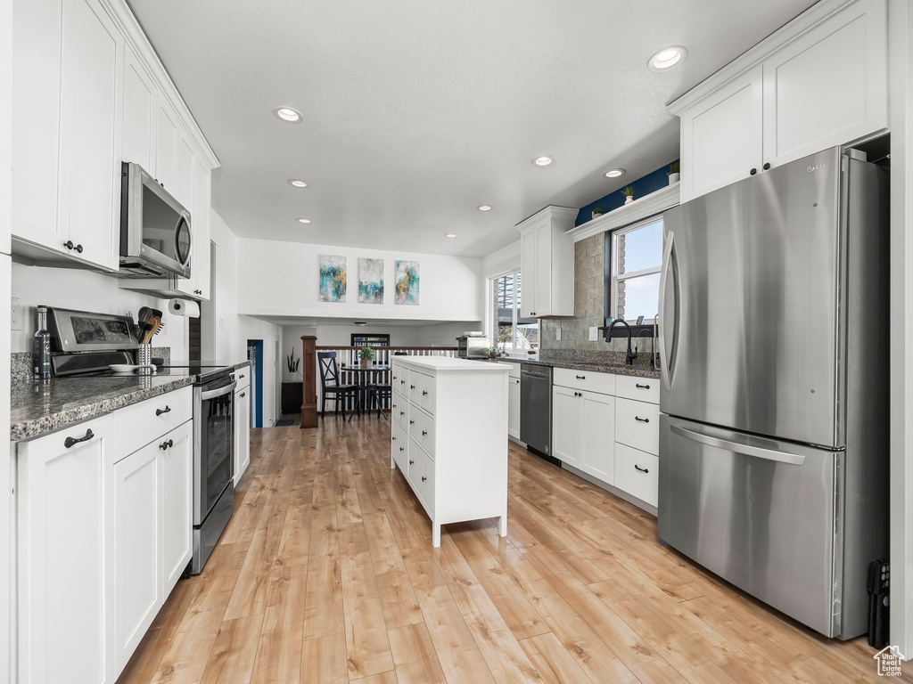 Kitchen featuring decorative backsplash, light wood-style flooring, white cabinets, and stainless steel appliances