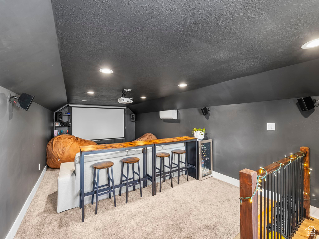 Carpeted home theater featuring a textured ceiling, recessed lighting, baseboards, a dry bar, and vaulted ceiling