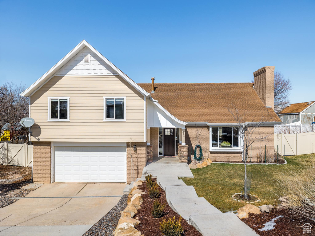 Tri-level home featuring brick siding, concrete driveway, a front lawn, and fence