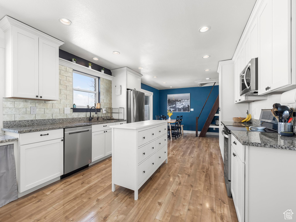 Kitchen with a kitchen island, appliances with stainless steel finishes, light wood-style flooring, and white cabinetry