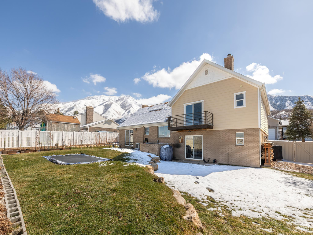 Rear view of house with a mountain view, a balcony, a fenced backyard, and a lawn