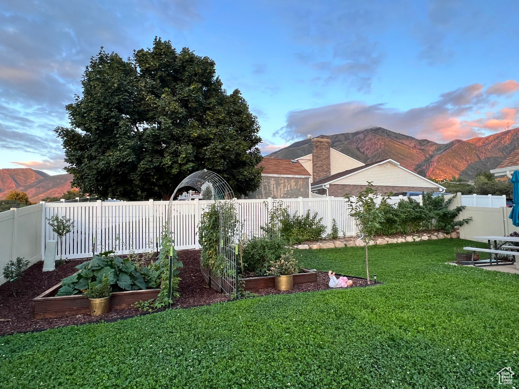 Yard at dusk with a garden, a mountain view, and a fenced backyard