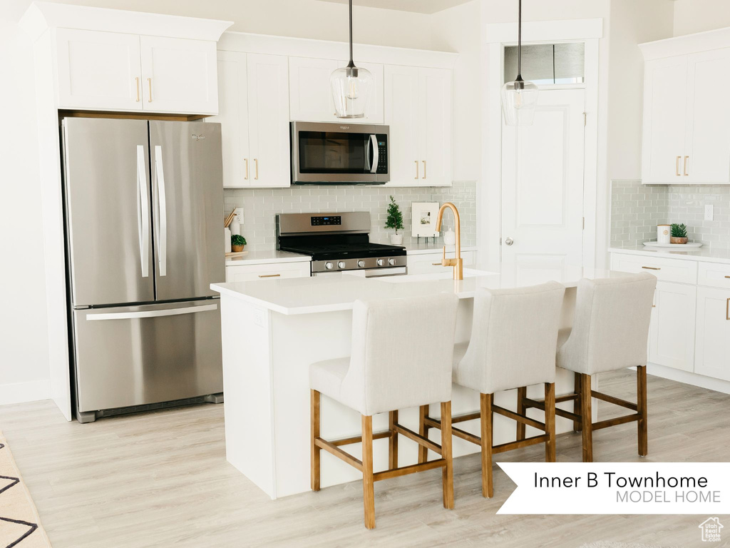 Kitchen featuring tasteful backsplash, light wood-style floors, appliances with stainless steel finishes, a breakfast bar area, and light countertops