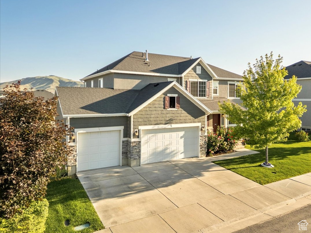 Craftsman inspired home featuring a garage, driveway, a front lawn, roof with shingles, and stone siding