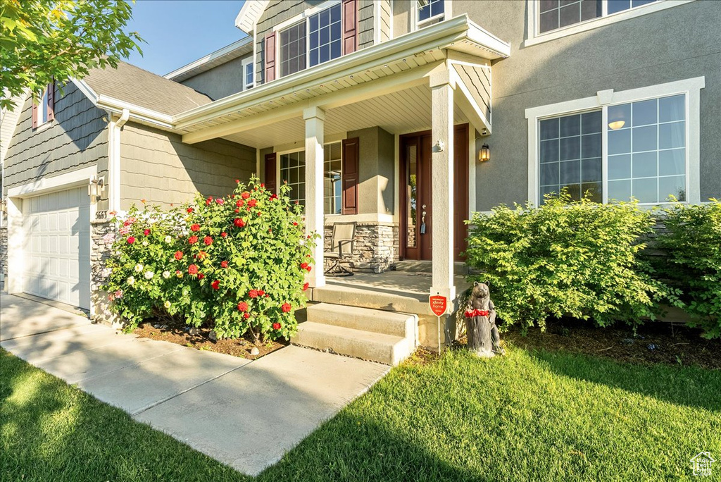 Doorway to property featuring covered porch, a garage, stone siding, and stucco siding