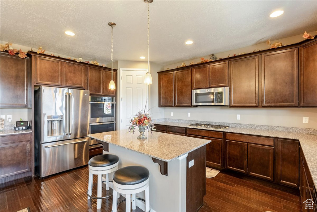 Kitchen featuring stainless steel appliances, dark wood-style flooring, a kitchen island, light stone countertops, and a breakfast bar area
