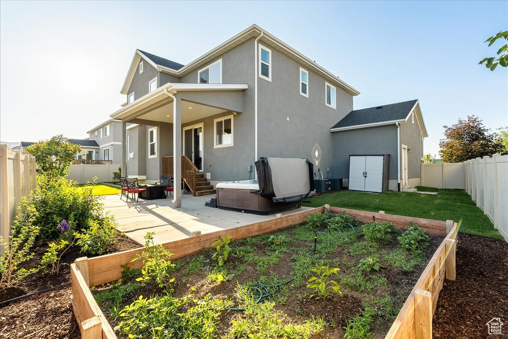 Back of house with a patio area, a garden, a hot tub, a fenced backyard, and stucco siding