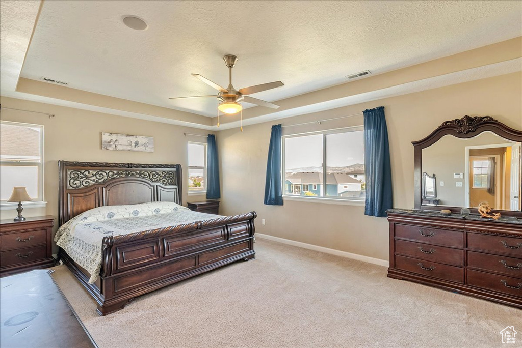 Bedroom featuring a tray ceiling, baseboards, light colored carpet, and a ceiling fan