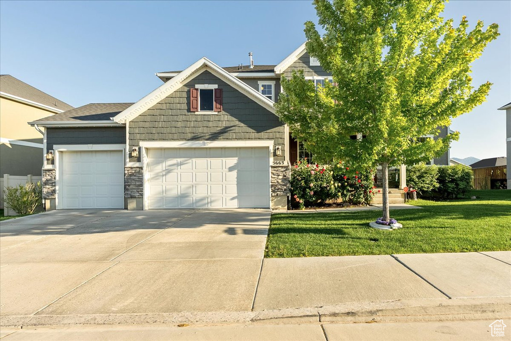 View of front of house featuring a garage, concrete driveway, stone siding, and a front lawn