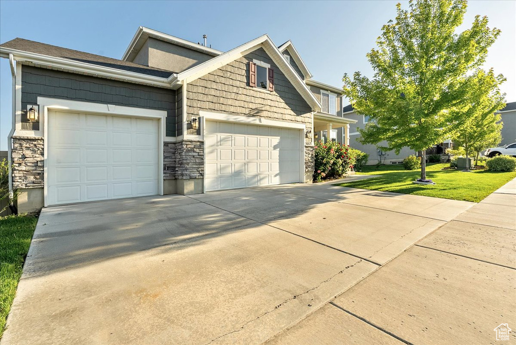 View of front of home with concrete driveway, stone siding, an attached garage, and a front lawn