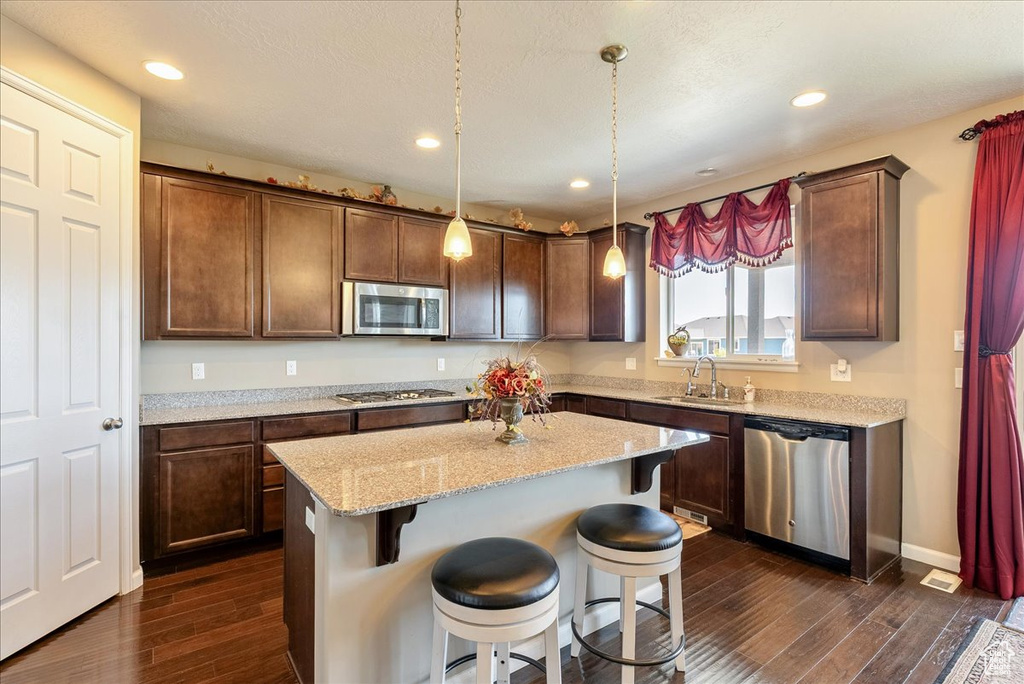 Kitchen with stainless steel appliances, dark wood-style floors, a kitchen breakfast bar, light stone counters, and recessed lighting