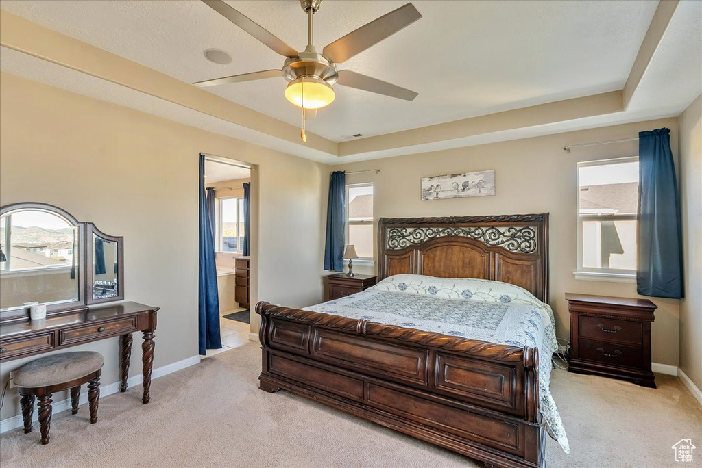 Bedroom with light colored carpet, baseboards, a raised ceiling, ensuite bath, and ceiling fan
