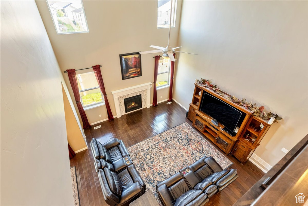 Living area with baseboards, a towering ceiling, wood finished floors, a glass covered fireplace, and ceiling fan