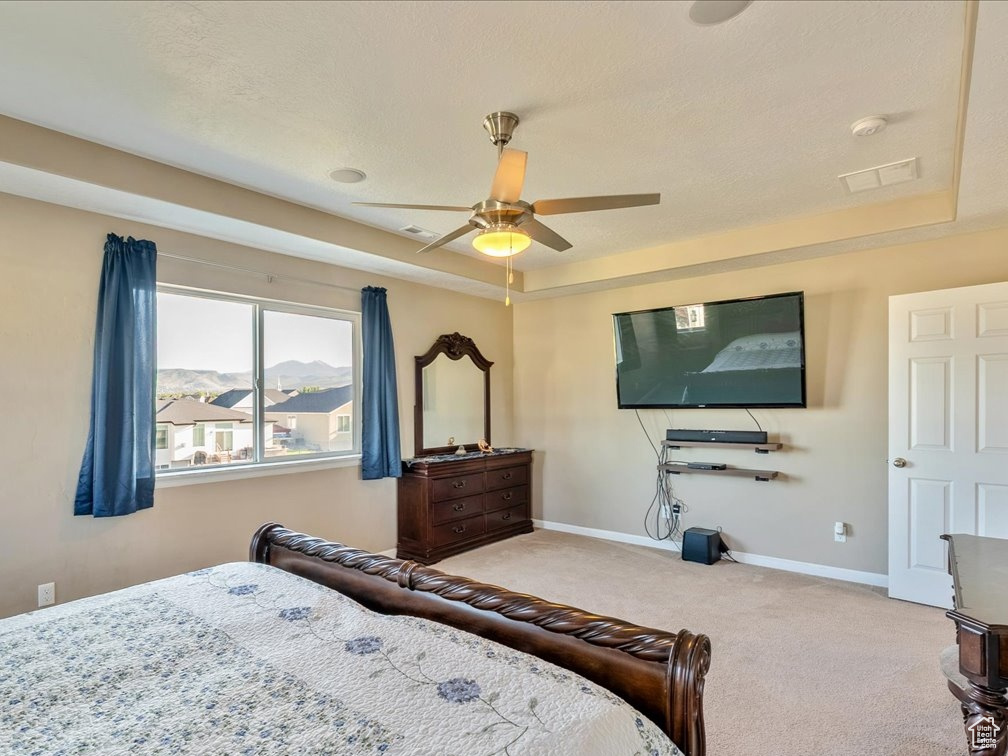 Bedroom featuring carpet, baseboards, a tray ceiling, and ceiling fan