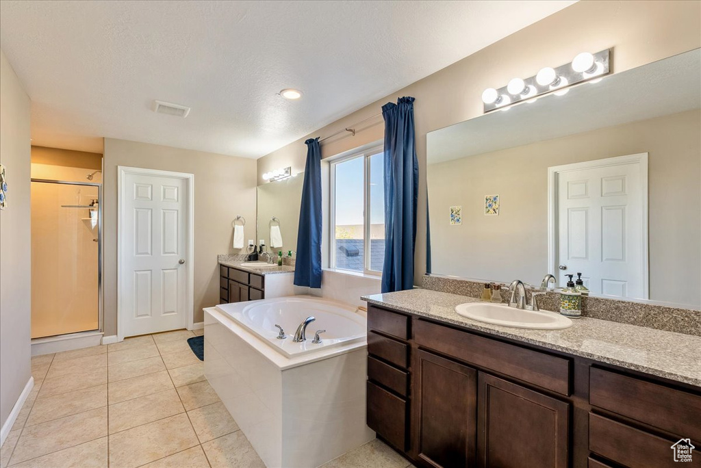 Bathroom featuring a garden tub, two vanities, a shower stall, tile patterned floors, and baseboards