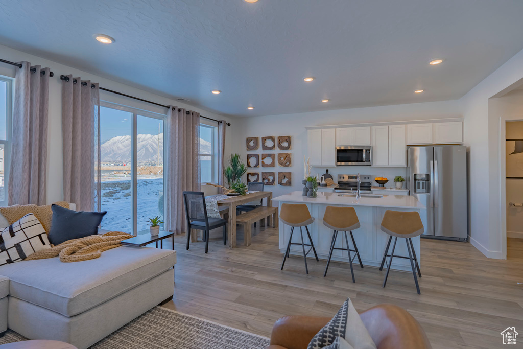 Kitchen with stainless steel appliances, a sink, white cabinetry, an island with sink, and a kitchen bar