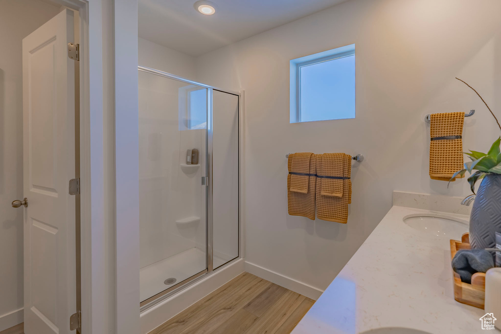 Bathroom with double vanity, wood finished floors, a stall shower, and a sink