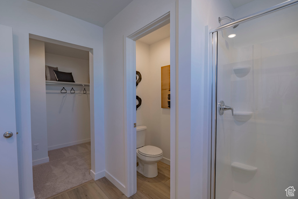 Full bath with a stall shower, baseboards, toilet, wood finished floors, and a spacious closet