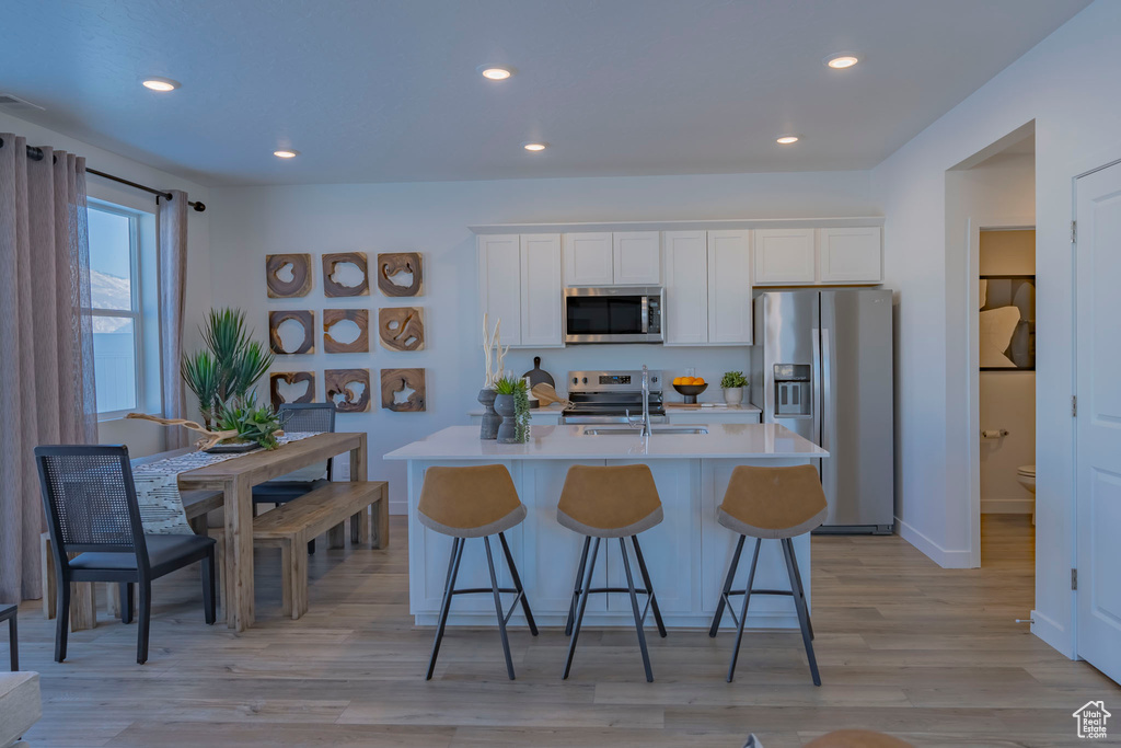 Kitchen featuring a center island with sink, stainless steel appliances, light countertops, a sink, and a kitchen bar