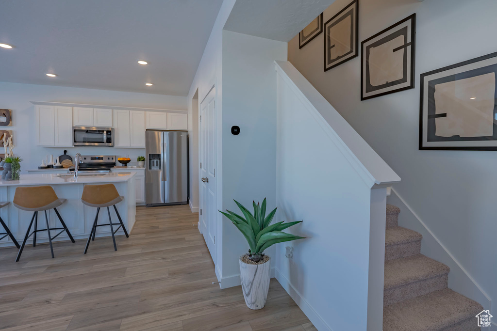 Kitchen featuring a breakfast bar area, stainless steel appliances, light countertops, light wood-style floors, and white cabinetry