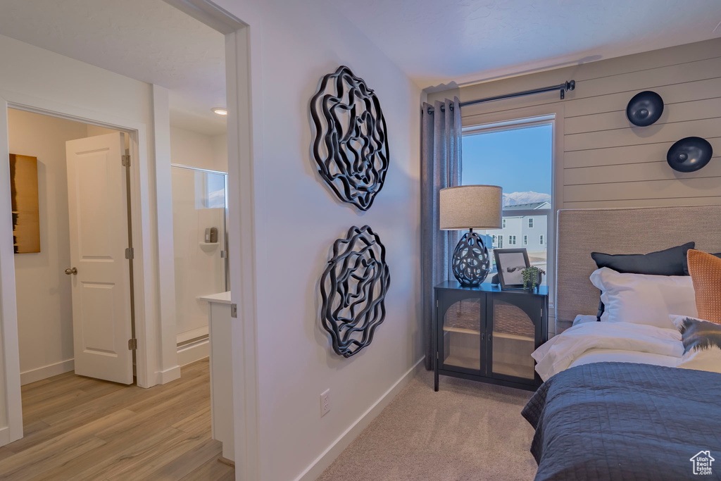 Bedroom with ensuite bathroom, light wood-style floors, and baseboards