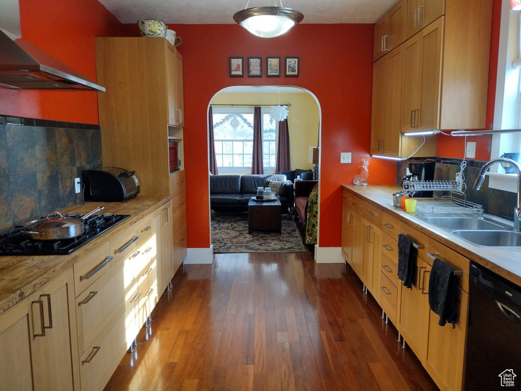 Kitchen with dark wood finished floors, arched walkways, black appliances, wall chimney exhaust hood, and a sink