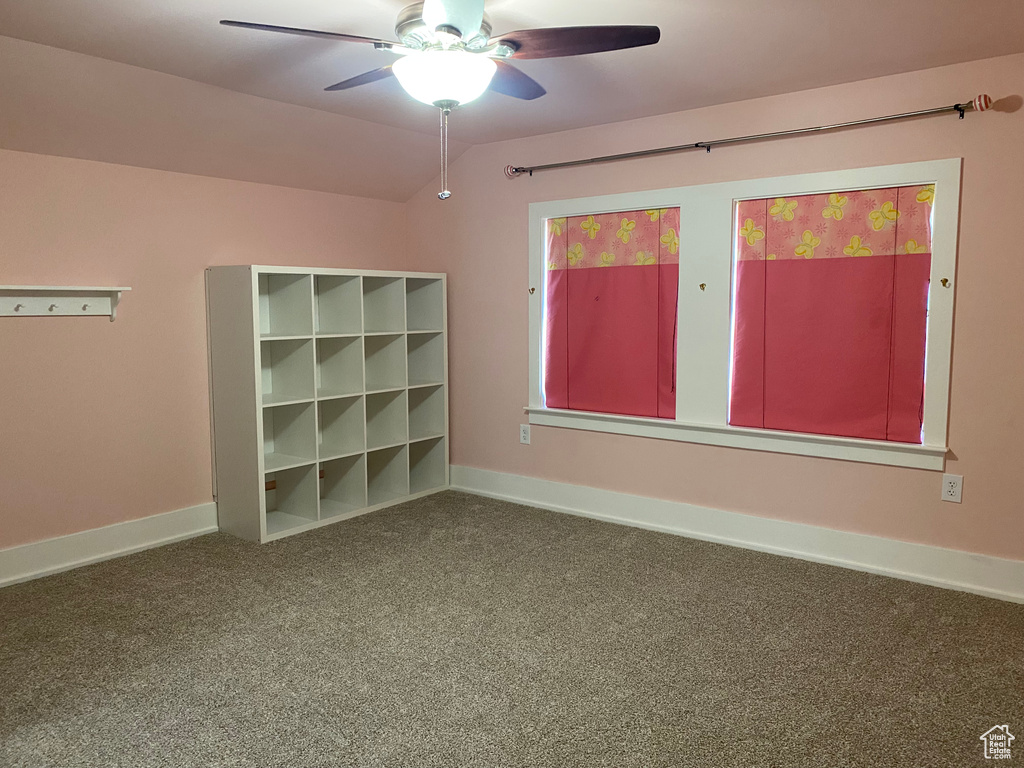 Carpeted empty room featuring vaulted ceiling, baseboards, and ceiling fan