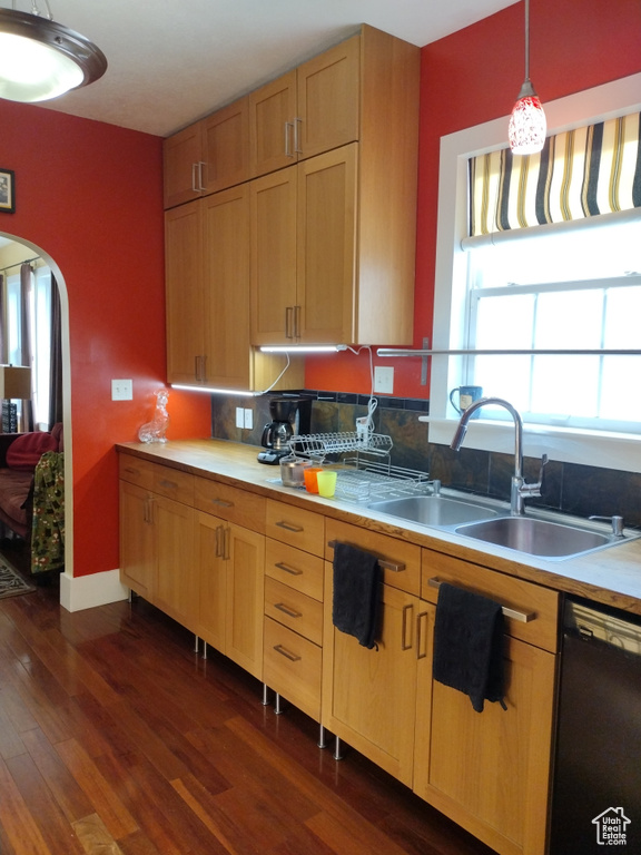 Kitchen with dark wood-type flooring, pendant lighting, black dishwasher, arched walkways, and a sink