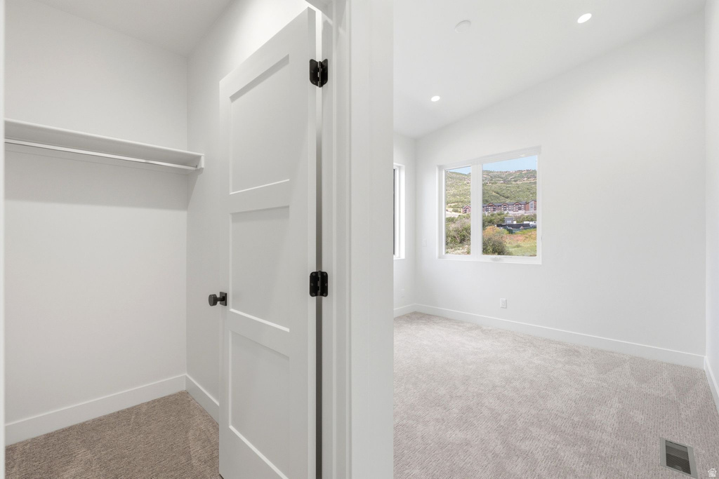 Recessed lighting illuminates a carpeted bedroom featuring a large window and a closet with a built-in shelf and hanging rod