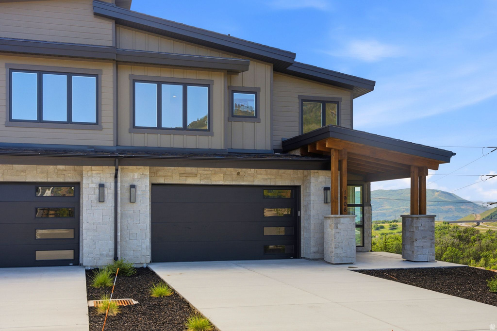 Contemporary facade featuring warm wood siding, stone accents, two integrated garages with modern doors, and a covered entry with timber columns