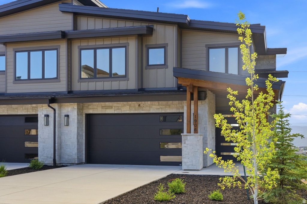 Contemporary exterior featuring dark gray garage doors, light-colored stone accents, and wood-toned siding