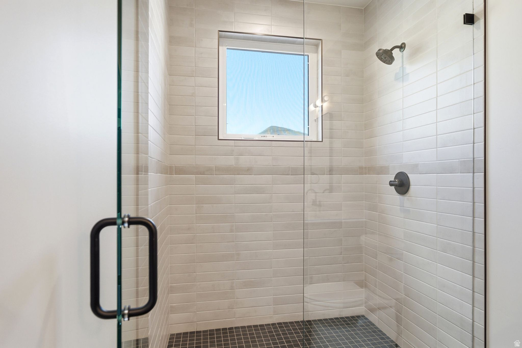 Modern shower enclosure featuring a frameless glass door with matte black hardware, light-toned horizontal tile walls, a rain showerhead, and dark mosaic tile flooring