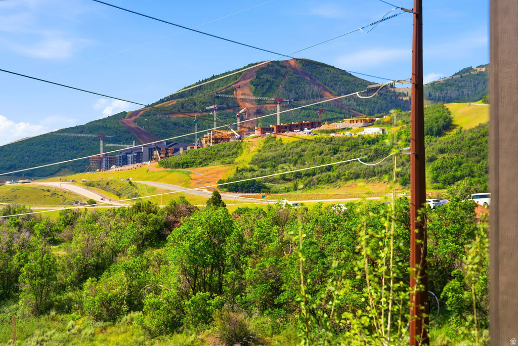 Mountain landscape featuring distant construction, a visible road, and foreground greenery