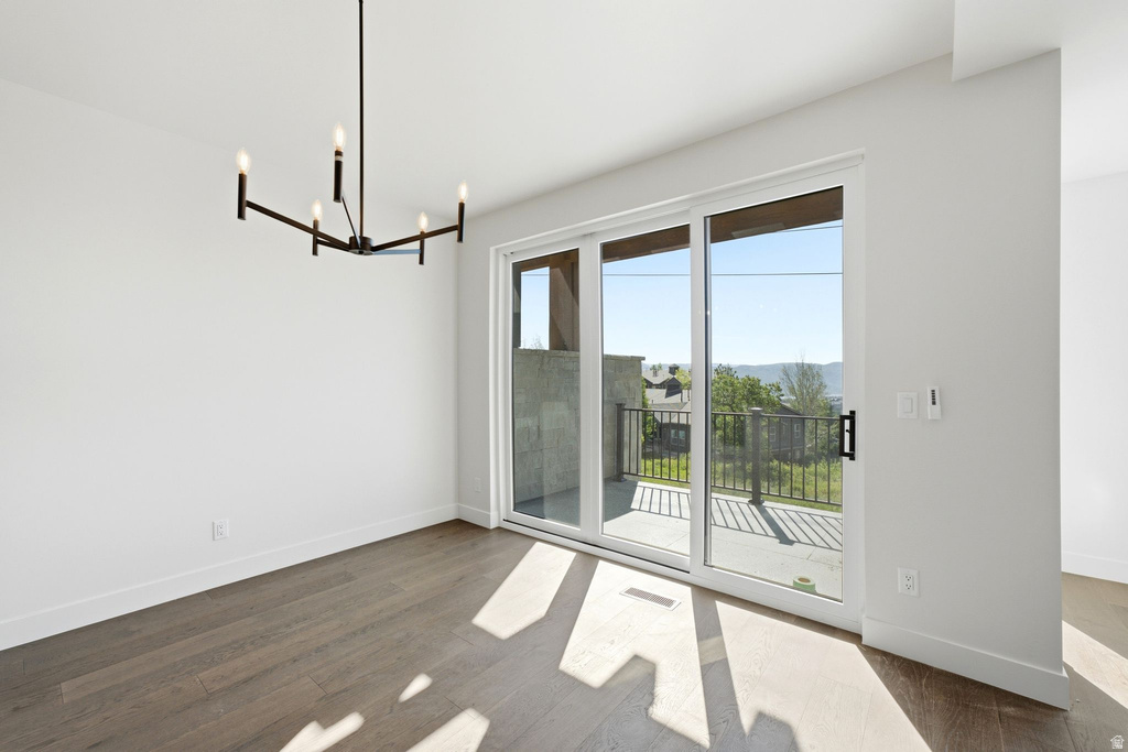 Spacious room with wood-finish flooring, a contemporary chandelier, and white baseboards