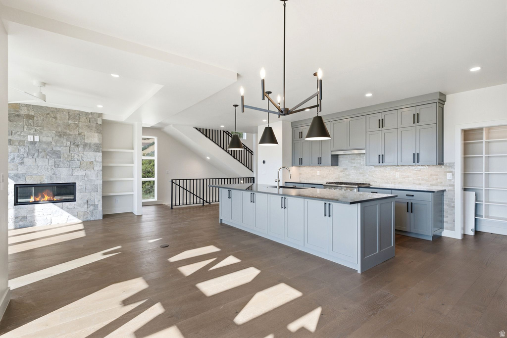 Spacious open-concept living area featuring wood-finish flooring, a stone-clad fireplace with built-in shelving, and an expansive kitchen island