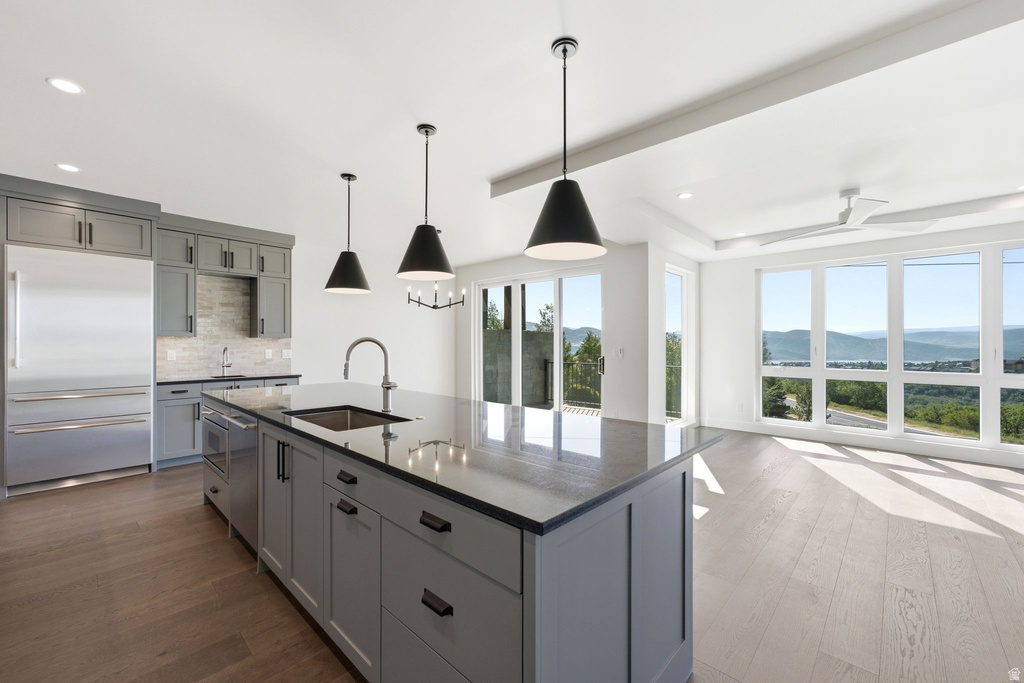 Modern kitchen featuring gray cabinetry, stainless steel appliances, and a central island with an integrated sink and pendant lighting