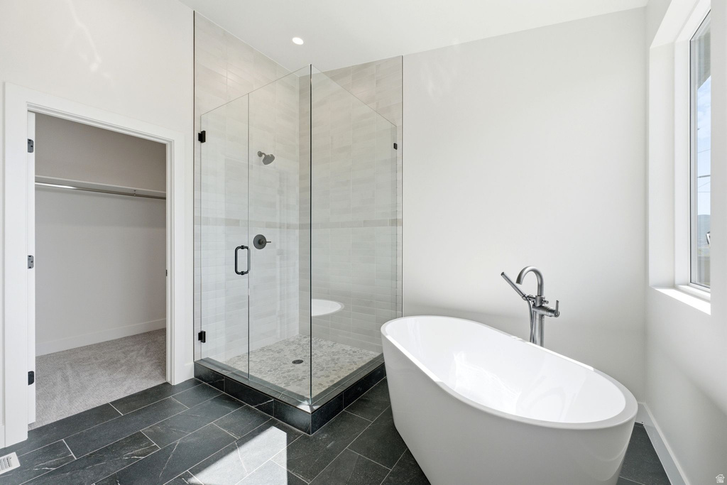 Freestanding soaking tub with chrome fixtures, glass-enclosed shower with tiled walls and pebble-finish floor, black slate-style tile flooring, and a large window providing natural light