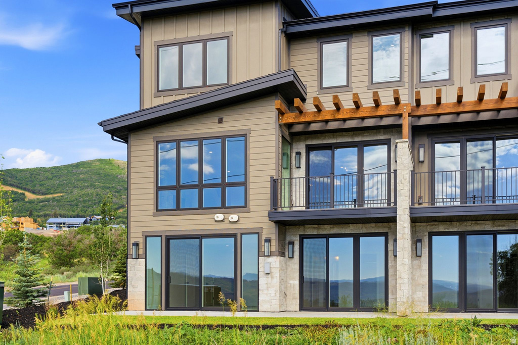Multi-level exterior featuring tan siding, dark window frames, and a prominent wooden pergola