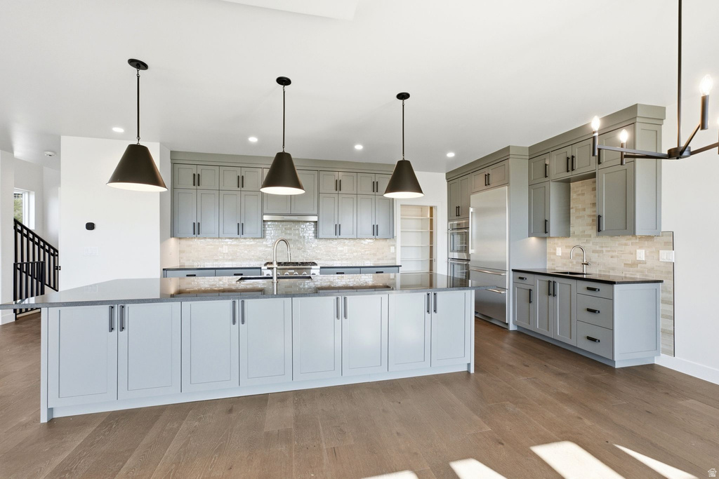 Contemporary kitchen featuring light gray cabinetry, stainless steel appliances, a large center island with pendant lighting, and wood-finish flooring