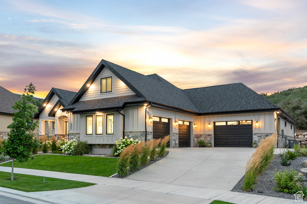 Modern inspired farmhouse with board and batten siding, a shingled roof, a garage, stone siding, and driveway