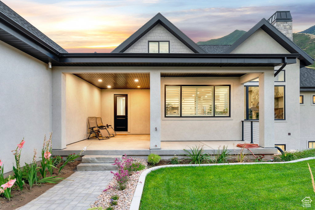 Exterior entry at dusk featuring covered porch, stucco siding, and a yard