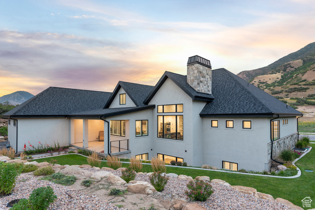 Back of property at dusk with stucco siding, a chimney, a mountain view, and a shingled roof