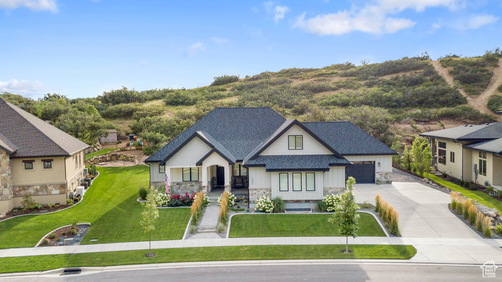 View of front of house featuring driveway, stone siding, a shingled roof, a front yard, and an attached garage